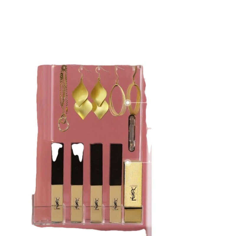 Cosmetic storage box displaying gold earrings and YSL lip gloss tubes on a pink background.