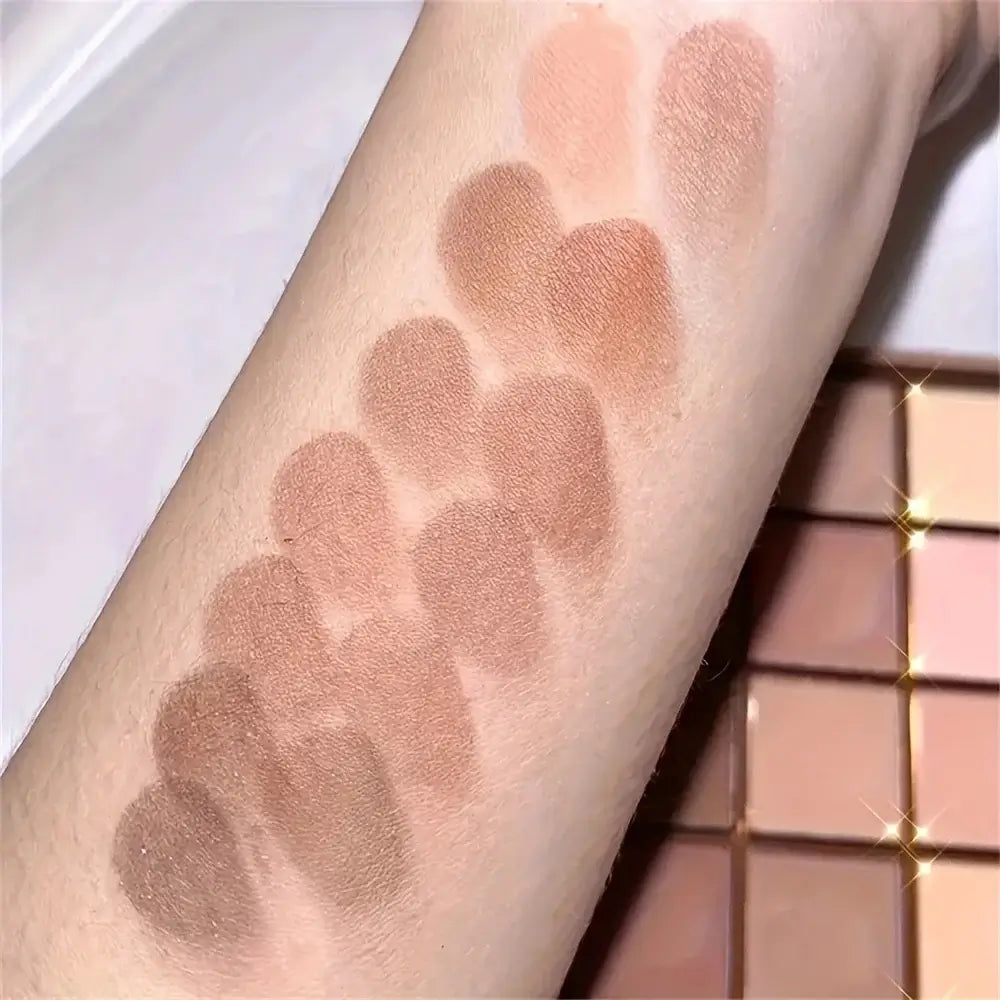 Swatches of neutral gray and brown earthy tones from a 25 color eyeshadow palette on an arm.