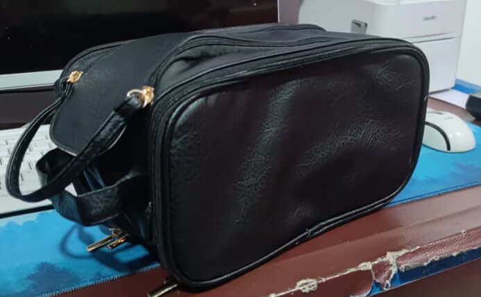 Stylish black double zipper cosmetic bag on a desk, perfect for household storage and travel.