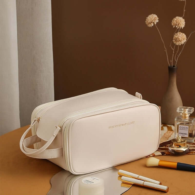 Stylish double zipper cosmetic bag in cream color on a table with brushes and decorative items.